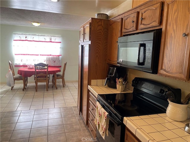 kitchen featuring black appliances, light tile patterned floors, and tile countertops