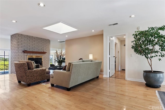 living room featuring a brick fireplace, a skylight, and light wood-type flooring