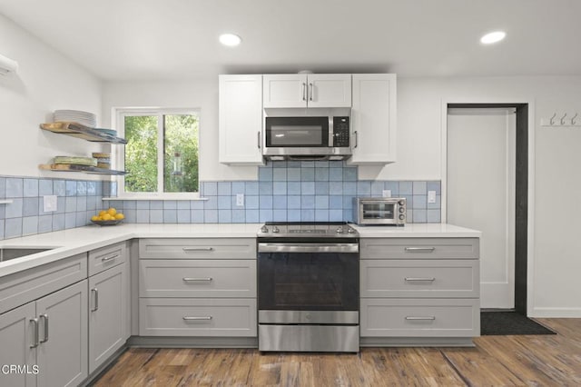 kitchen with appliances with stainless steel finishes, tasteful backsplash, dark wood-type flooring, and gray cabinetry