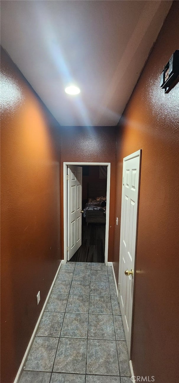 hallway featuring vaulted ceiling and dark tile patterned flooring