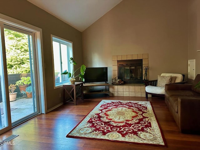 living room featuring lofted ceiling, a tiled fireplace, and hardwood / wood-style flooring