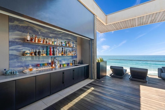 bar with light hardwood / wood-style floors, backsplash, a water view, and sink