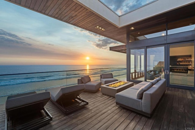 deck at dusk with a water view, an outdoor living space, and a beach view