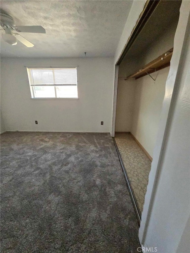 unfurnished bedroom with a textured ceiling, dark colored carpet, ceiling fan, and a closet