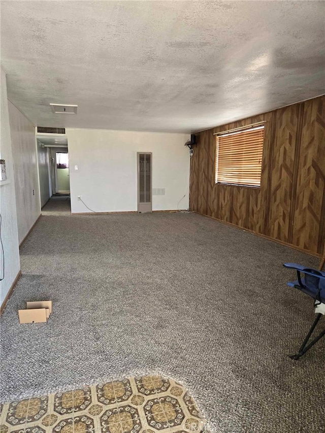 spare room with a textured ceiling, carpet flooring, and wood walls