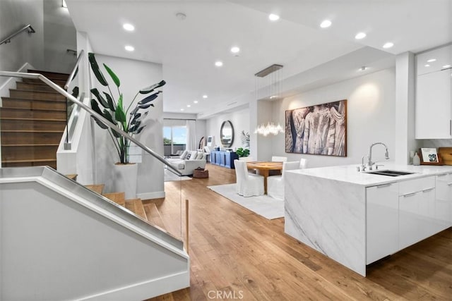 interior space featuring white cabinets, light hardwood / wood-style floors, decorative light fixtures, and sink