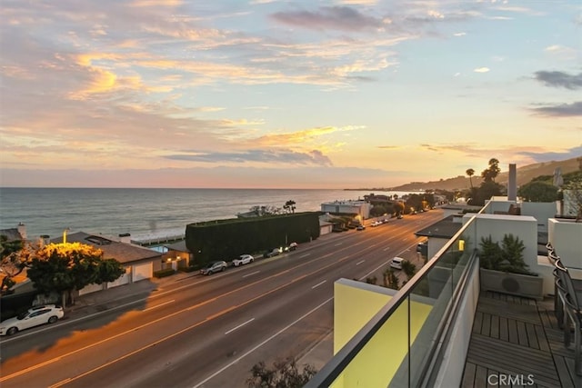 balcony at dusk featuring a water view