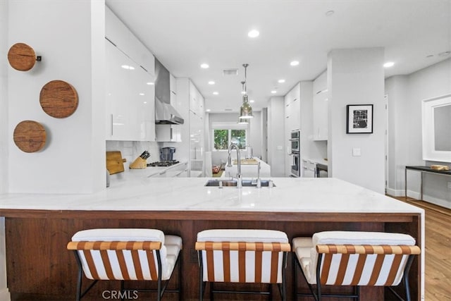 kitchen featuring white cabinets, sink, kitchen peninsula, a breakfast bar area, and light hardwood / wood-style floors