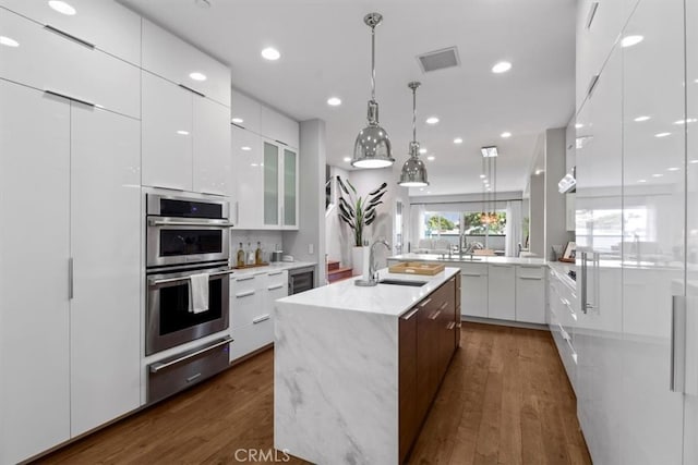 kitchen featuring sink, a center island with sink, white cabinetry, double oven, and dark hardwood / wood-style flooring