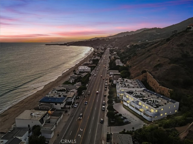 aerial view at dusk featuring a water and mountain view and a beach view