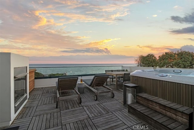 deck at dusk with a water view and a hot tub