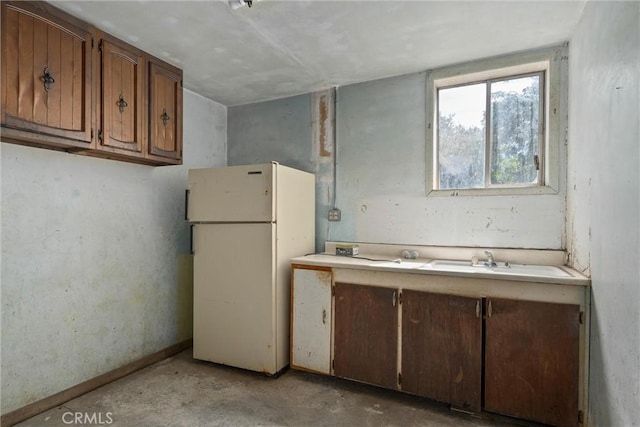 kitchen with a sink, brown cabinets, concrete flooring, light countertops, and freestanding refrigerator