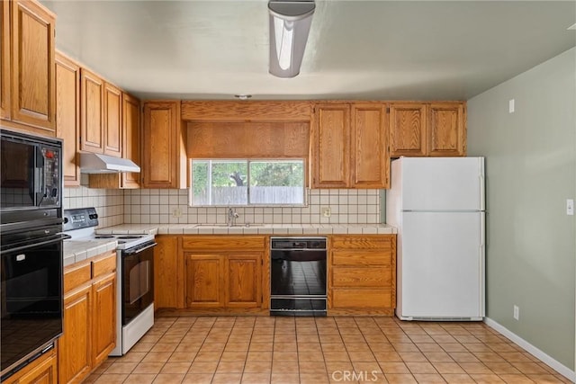 kitchen with tile counters, a sink, black appliances, backsplash, and under cabinet range hood