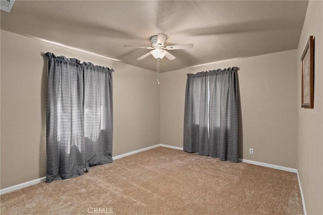 carpeted spare room with visible vents, a ceiling fan, and baseboards