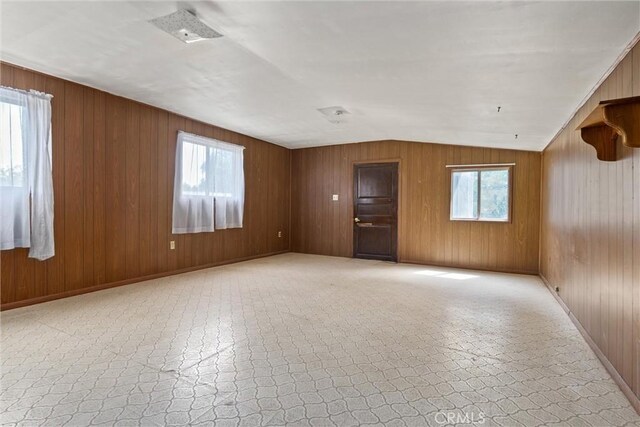 empty room with lofted ceiling, wood walls, and baseboards