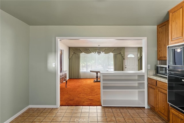 kitchen featuring light colored carpet, an inviting chandelier, tile countertops, and black double oven