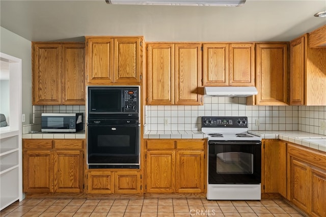 kitchen featuring light tile patterned flooring, tile countertops, backsplash, and black appliances