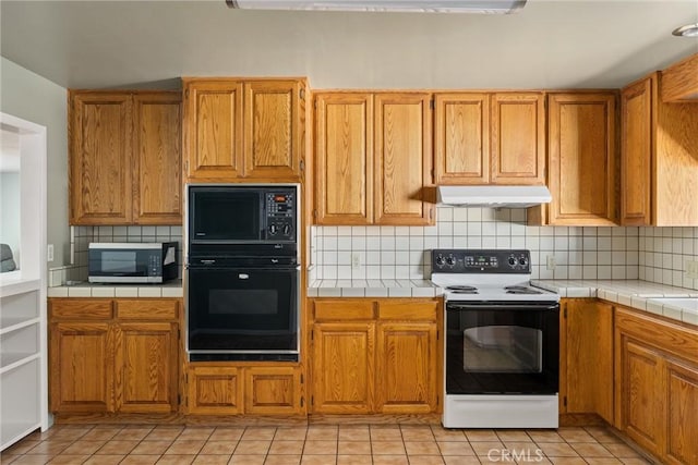 kitchen featuring backsplash, under cabinet range hood, tile countertops, and black appliances