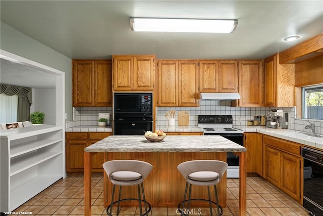 kitchen with black appliances, decorative backsplash, under cabinet range hood, and a sink