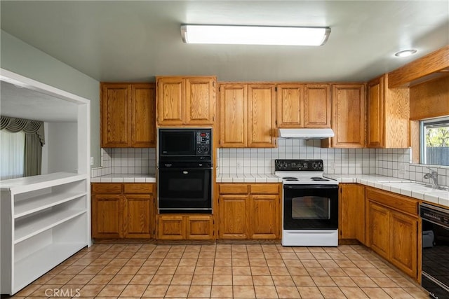 kitchen with a sink, decorative backsplash, tile counters, under cabinet range hood, and black appliances