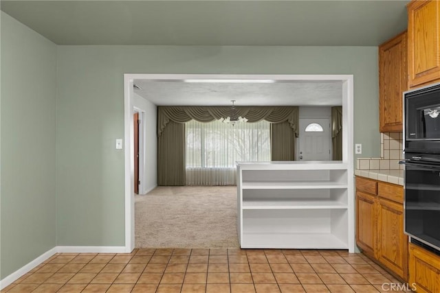 kitchen with tile countertops, brown cabinets, light tile patterned floors, an inviting chandelier, and light carpet