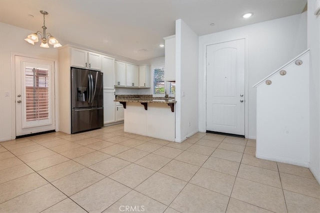 kitchen with a kitchen breakfast bar, white cabinets, stainless steel refrigerator with ice dispenser, and decorative light fixtures