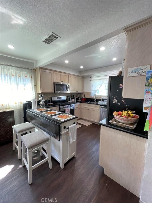 kitchen featuring sink, a textured ceiling, appliances with stainless steel finishes, dark hardwood / wood-style floors, and light brown cabinetry