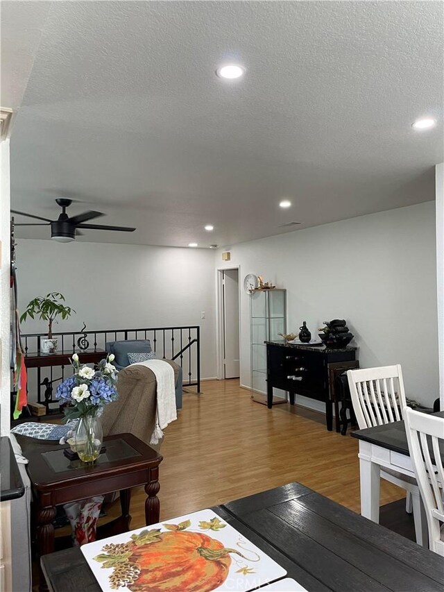 living room with ceiling fan, a textured ceiling, and light hardwood / wood-style flooring