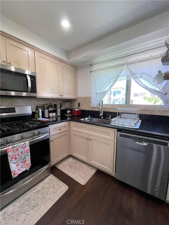 kitchen with light brown cabinets, sink, backsplash, dark wood-type flooring, and stainless steel appliances