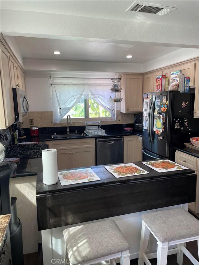 kitchen with sink, black appliances, a breakfast bar, light brown cabinetry, and decorative backsplash