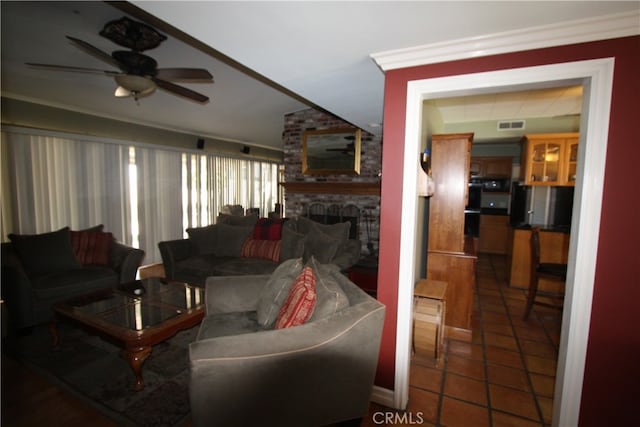 living room featuring crown molding, a large fireplace, ceiling fan, and dark tile patterned floors