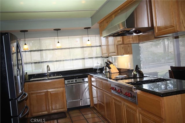 kitchen featuring dark countertops, wall chimney exhaust hood, appliances with stainless steel finishes, pendant lighting, and a sink