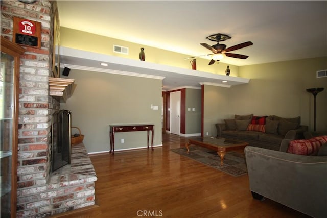 living room with ceiling fan, visible vents, wood finished floors, and ornamental molding