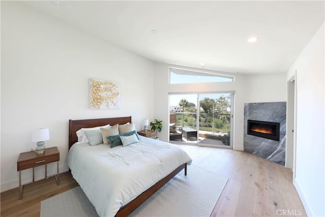 bedroom with access to exterior, light hardwood / wood-style flooring, a fireplace, and lofted ceiling