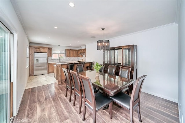 dining room with a notable chandelier, a healthy amount of sunlight, light wood-type flooring, and crown molding