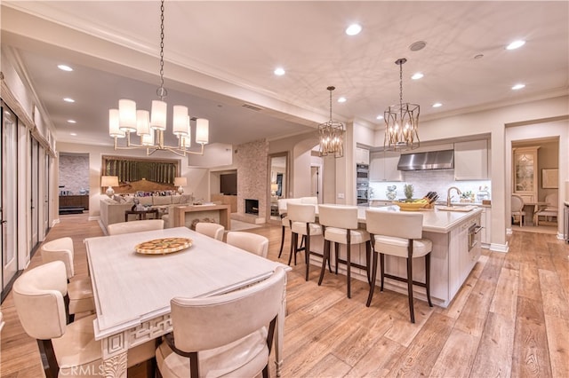 dining space featuring sink, light wood-type flooring, ornamental molding, and a large fireplace