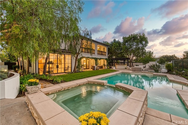 pool at dusk featuring an in ground hot tub and a patio area