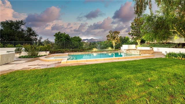 pool at dusk featuring a jacuzzi, a lawn, and a patio area