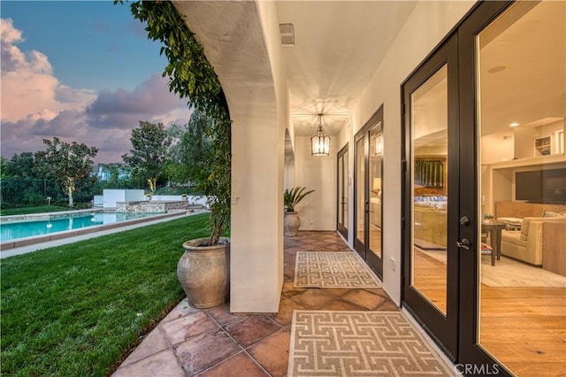 patio terrace at dusk featuring an outdoor pool, visible vents, a lawn, and french doors