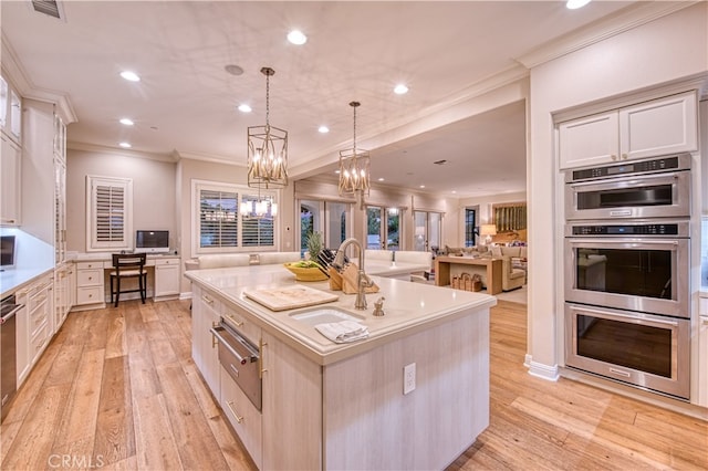 kitchen featuring a large island with sink, double oven, light hardwood / wood-style flooring, and decorative light fixtures