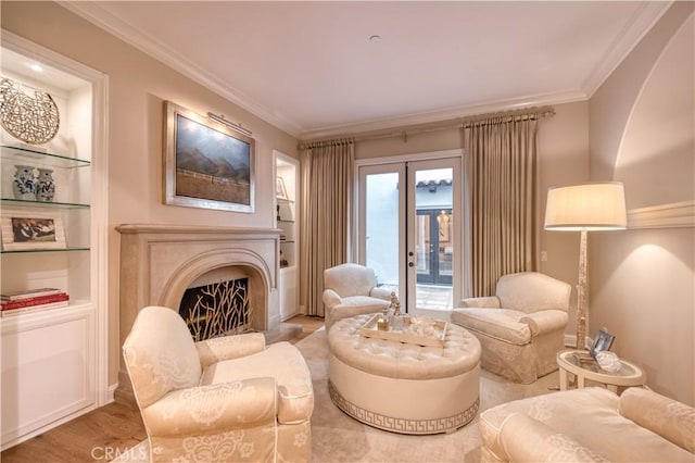 sitting room featuring wood finished floors, built in shelves, a lit fireplace, and ornamental molding