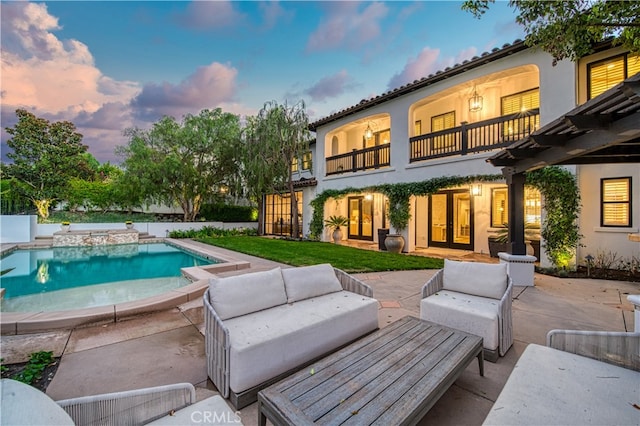 back house at dusk with a balcony, an outdoor living space, and a patio