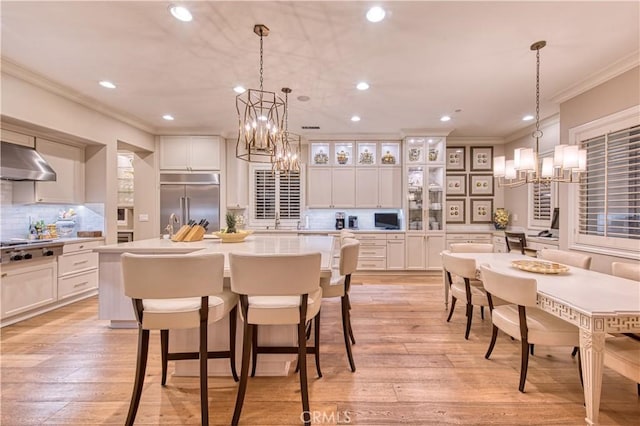 kitchen with light wood-style flooring, ornamental molding, stainless steel appliances, white cabinets, and a chandelier