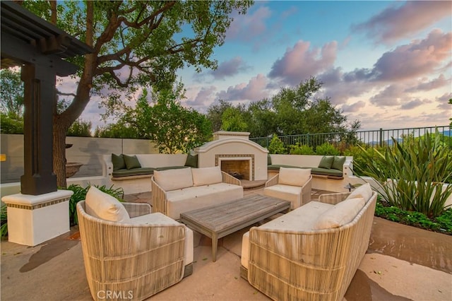 patio terrace at dusk with an outdoor living space with a fireplace and fence