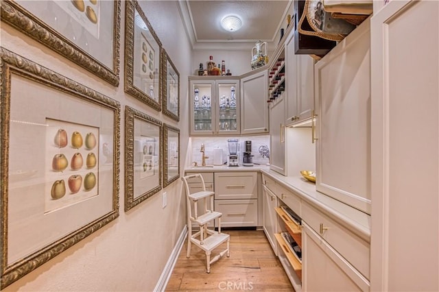 interior space with decorative backsplash, crown molding, light wood-type flooring, and a sink