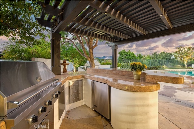 patio terrace at dusk featuring an outdoor kitchen, a pergola, and a grill