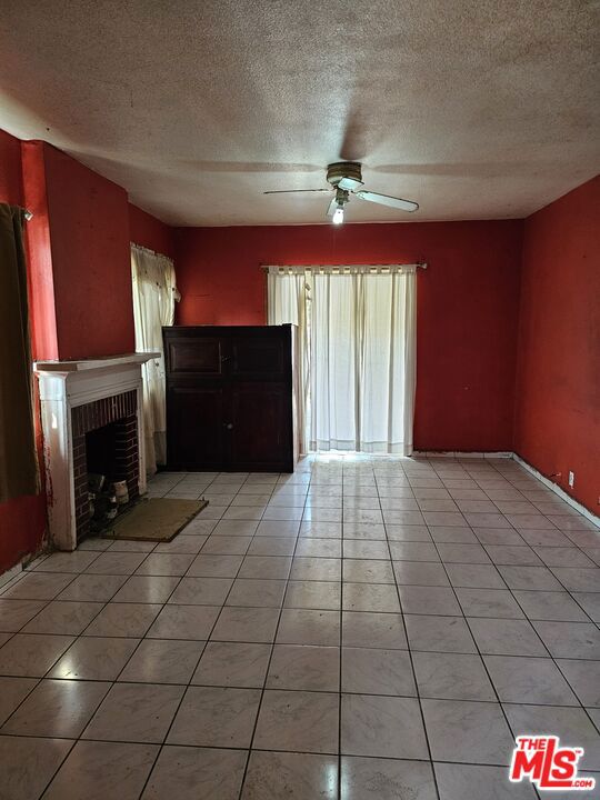 unfurnished living room with light tile patterned flooring, a textured ceiling, ceiling fan, and a fireplace