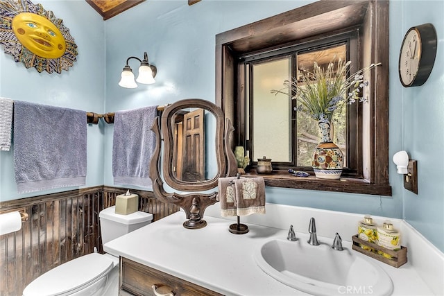 bathroom featuring vanity, wooden walls, and toilet