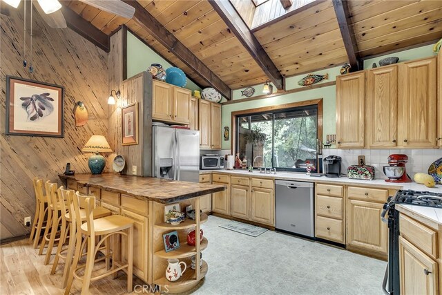 kitchen with a breakfast bar area, wood walls, beam ceiling, a skylight, and appliances with stainless steel finishes