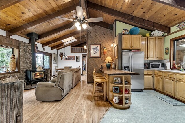 kitchen featuring stainless steel appliances, lofted ceiling with beams, a wood stove, and light hardwood / wood-style flooring